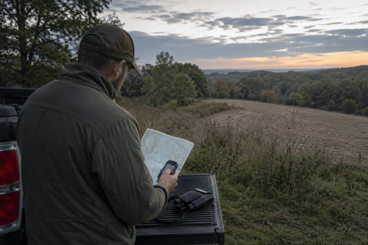 A hunter studies a topographic map beside a wooded ridge before deer season.